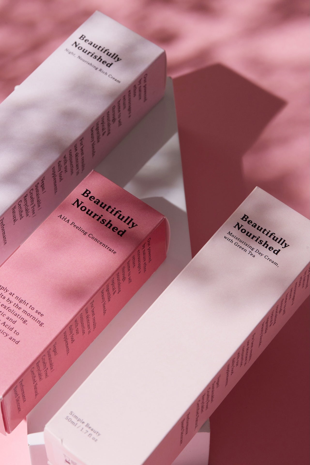 natural vegan skincare products and packaging with 'Beautifully Nourished' branding on a pink background.