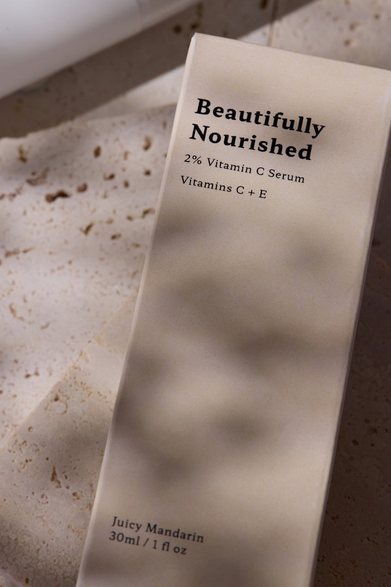 Skincare serum bottle labeled 'Beautifully Nourished' on a textured surface for bright skin