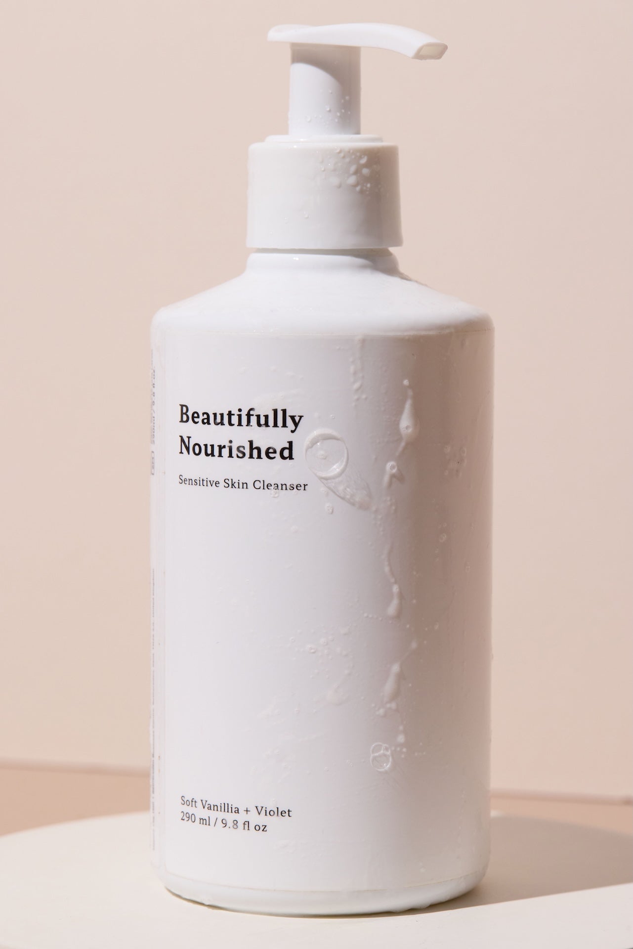White bottle of Beautifully Nourished violet and vanilla sensitive skin cleanser for soft, refreshed skin on a beige background