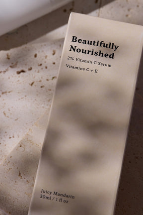 Skincare serum bottle labeled 'Beautifully Nourished' on a textured surface for bright skin